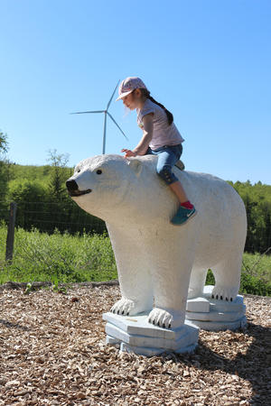 Ein Mädchen sitzt auf einer Eisbärstatue, im Hintergrund ist eine der Windenergieanlagen von Weilrod zu sehen.