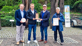Drei Männer und eine Frau zeigen die Urkunde, Trophäe und Plakette der Auszeichnung "Streuobstkommune 2022".