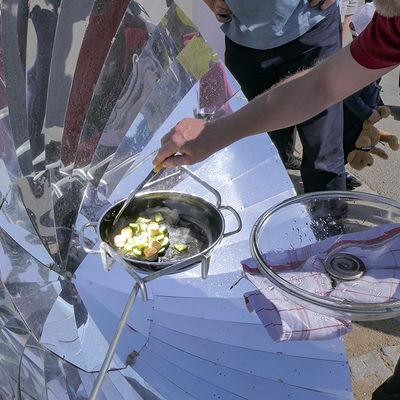 Zucchini und Tofuwürstchen werden auf einem Solarkocher gekocht und umgerührt.