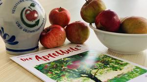 Das Magazin "Der Apfelbote" liegt auf dem Tisch zwischen Steuobst-Äpfeln und einen Bempel mit dem Logo der Apfelwein- und Obstwiesenroute.