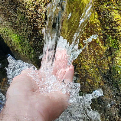 Hand fängt Wasser am Brunnen auf.
